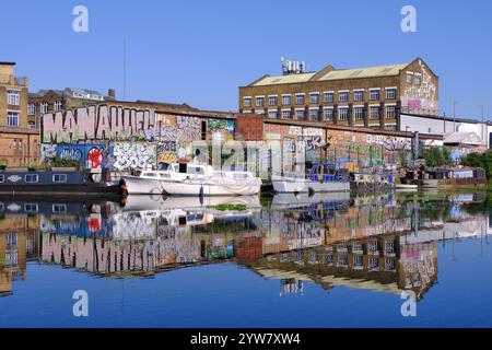 Graffitis colorés (Street art), bateaux sur le canal, péniches, bâtiments industriels avec des reflets miroirs sur la rivière Lee navigation à Stratford, Londres Banque D'Images