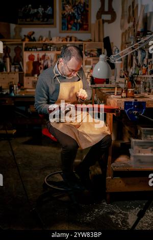 Cremona, Italie - 9 décembre 2024 - Luca Tenore maître luthier italien travaille sur un violon dans son atelier, appliquant soigneusement le vernis avec un brus Banque D'Images