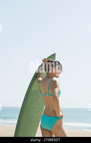 Femme dans la vingtaine portant une combinaison tenant une planche de surf Banque D'Images
