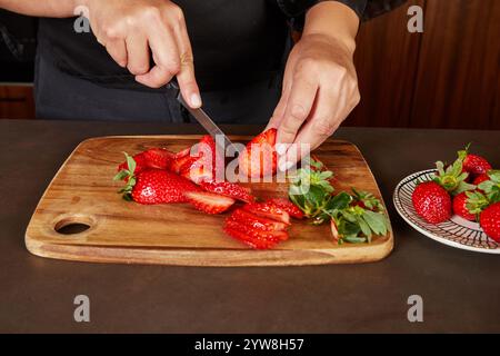 Une personne tranche des fraises mûres sur une planche de bois, préparant des fruits frais pour une recette ou servant de garniture. Banque D'Images