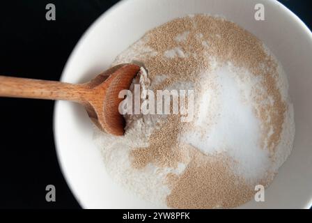 Levure, sel et farine dans un bol avec une cuillère en bois sur un fond rustique, prêt pour la cuisson du pain Banque D'Images