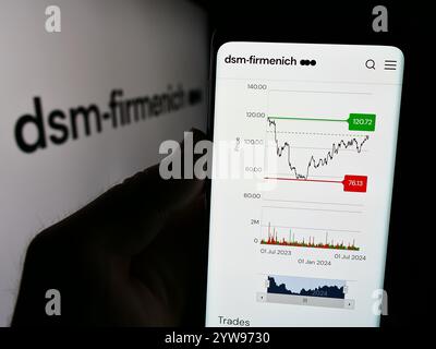 Dans cette illustration photo, une personne tient un téléphone portable avec la page Web de la société chimique suisse DSM-Firmenich AG devant le logo de l'entreprise. Banque D'Images