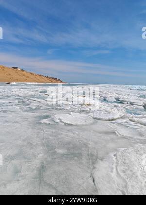 La glace gelée s'étend à travers l'eau vers des collines sablonneuses sous un ciel bleu vif un jour d'hiver. Banque D'Images