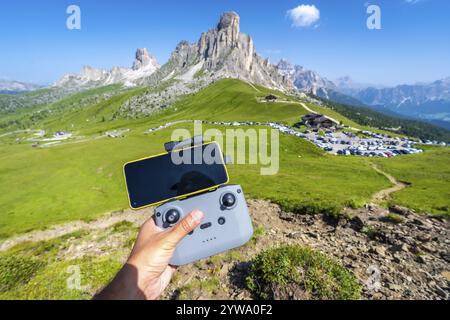 Piloter à la main un drone avec un smartphone attaché au contrôleur dans le paysage pittoresque du col de giau, dolomites, italie, pendant une journée d'été ensoleillée Banque D'Images