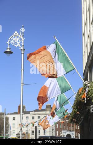 Drapeaux tricolores irlandais soufflant dans la brise à l'extérieur d'un pub dans une rue principale. Dublin, Irlande, Europe Banque D'Images