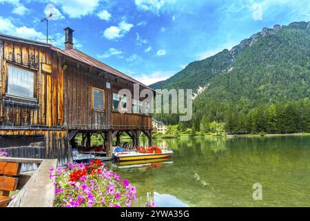 Pédalos amarrés sous une charmante maison en bois sur les eaux calmes du lac dobbiaco, avec les superbes dolomites en vue Banque D'Images