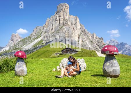 Mère et enfant se relaxant près des champignons en bois, profitant d'une vue imprenable sur le col de giau et les sommets environnants des dolomites lors d'une journée d'été ensoleillée Banque D'Images