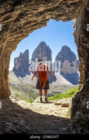 Randonneur profitant de la vue imprenable sur Tre cime di lavaredo, un symbole des dolomites, de l'intérieur d'une grotte de Tre Cime lors d'une randonnée estivale Banque D'Images