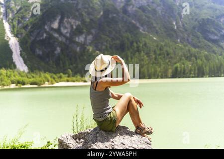 Femme portant un chapeau de paille assis sur un rocher contemplant le magnifique paysage du lac Durrensee dans les dolomites italiennes pendant l'été Banque D'Images