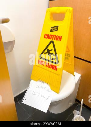 Un sol mouillé est placé au-dessus d'une toilette dans une cabine avec une note manuscrite indiquant que la toilette ne fonctionne pas. Banque D'Images