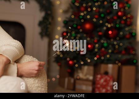 main féminine tenant des étincelles contre fond d'arbre de noël de près, joyeux noël. Banque D'Images
