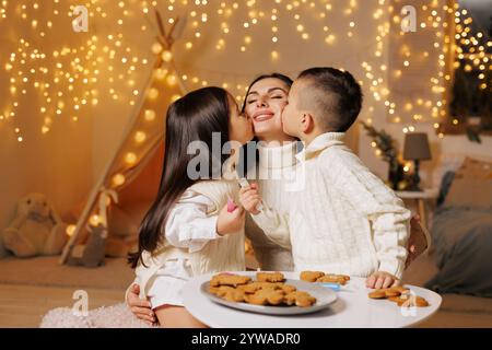 deux enfants embrassant la mère le soir de noël dans une chambre confortable, famille heureuse à noël, Banque D'Images