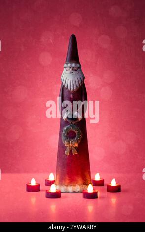 Une nature morte de Noël d'un ornement Père Noël entouré d'illuminations de lumière de thé et un fond rouge. Banque D'Images