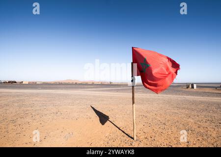 Un drapeau national du Maroc bat au vent au milieu d'un village nomade dans le désert marocain. Vous pouvez voir la couleur rouge du tissu et Banque D'Images