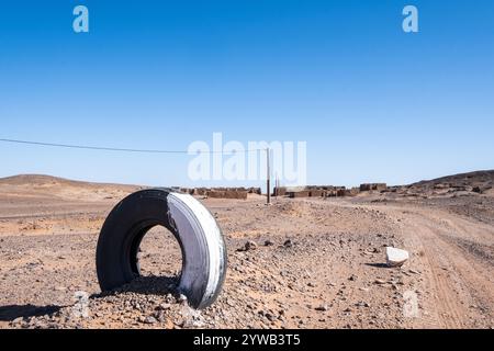 Un vieux pneu peint à la chaux blanche marque la route d'entrée d'une petite ville au milieu du désert marocain en Afrique du Nord. C'est un pop épars Banque D'Images