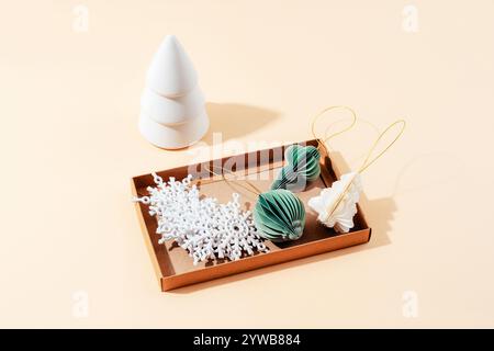 Une configuration minimaliste de décorations de Noël, sapin de Noël en céramique et flocons de neige, ornements dans une boîte. Vue de dessus Banque D'Images
