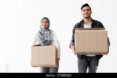 Une famille musulmane joyeuse tenant des fournitures de déménagement dans un appartement vide Banque D'Images