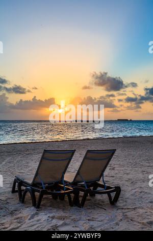 Deux chaises de plage sont face à l'océan, avec le coucher de soleil en arrière-plan. Les chaises sont vides, et la scène est paisible et sereine Banque D'Images