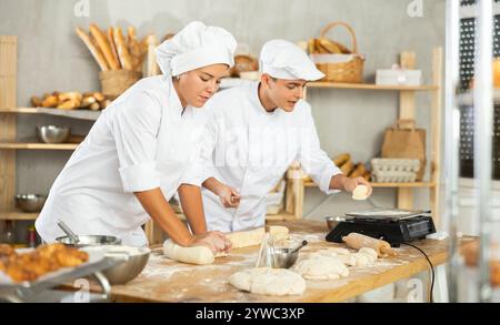 Les boulangers filles et gars coupent de petits morceaux de pâte à partir de gros morceaux et les mettent sur des écailles. Banque D'Images