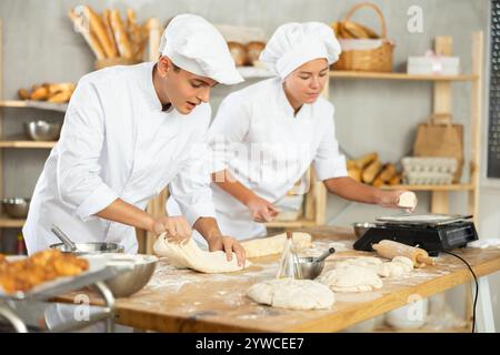 Les boulangers filles et gars coupent de petits morceaux de pâte à partir de gros morceaux et les mettent sur des écailles. Banque D'Images