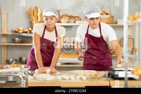 Les boulangers filles et gars coupent de petits morceaux de pâte à partir de gros morceaux et les mettent sur des écailles. Banque D'Images