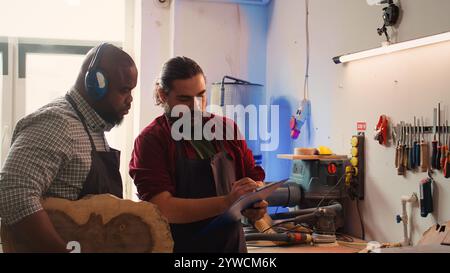 Artisan et collègue regardent sur les schémas techniques pour fabriquer un objet en bois commandé. Fabricant et collègue analysent les plans pour exécuter le projet de menuiserie d'assemblage de meubles, caméra B. Banque D'Images