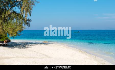 De douces vagues se tapissent contre le sable immaculé de l'île de Koh Munnork, baignée de soleil, d'eaux turquoises sous un ciel bleu clair, invitant à la détente et à l'aventure en Thaïlande. Banque D'Images