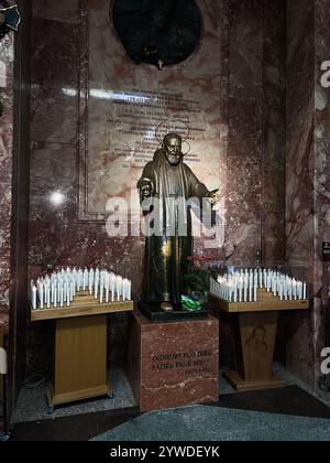 San Giovanni Rotondo, Italie - 13 juillet 2022 : une statue en bronze de Padre Pio entourée de nombreuses bougies allumées dans un sanctuaire en marbre, créant un lieu serein et serein Banque D'Images