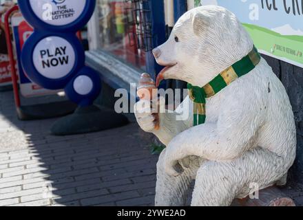 Ironbridge, Shropshire, Royaume-Uni, 22-06-2018. Un ours blanc modèle est assis sur une bûche mangeant de la crème glacée lors d'une chaude journée d'été. Devant le magasin de crème glacée Banque D'Images