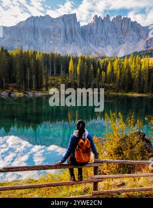 Un voyageur au bord d'un lac étincelant niché dans les Dolomites, entouré d'un feuillage d'automne vibrant et de montagnes majestueuses reflétant dans l'eau. Lac Carezza ou Karersee en Italie saison d'automne Banque D'Images