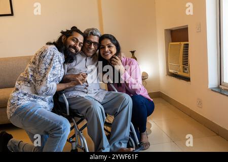 Heureux jeune couple indien passant du temps de qualité avec un père handicapé en fauteuil roulant à la maison. concept de fête des parents ou de fête des pères. Banque D'Images