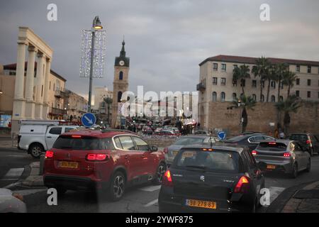 Jaffa, circulation dense en fin d'après-midi vu à travers un pare-brise de voiture, la Tour de l'horloge, vieilles maisons, voitures, palmiers Washingtonia et lampadaires. Banque D'Images