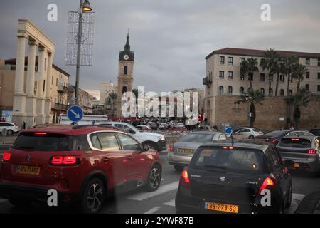 Jaffa, circulation dense en fin d'après-midi vu à travers un pare-brise de voiture, la Tour de l'horloge, vieilles maisons, voitures, palmiers Washingtonia et lampadaires. Banque D'Images