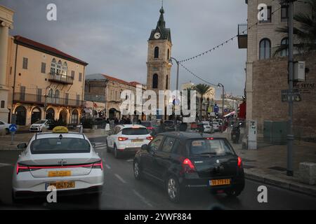 Jaffa, circulation dense en fin d'après-midi vu à travers un pare-brise de voiture, la Tour de l'horloge, vieilles maisons, voitures, palmiers Washingtonia et lampadaires. Banque D'Images