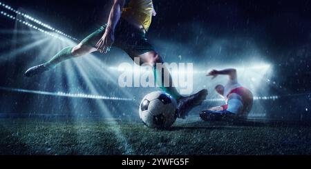 Deux joueurs de football compétitifs en mouvement essaient de garder la défense dans un stade humide pendant un match de football décisif. Effet de flou de mouvement. Banque D'Images