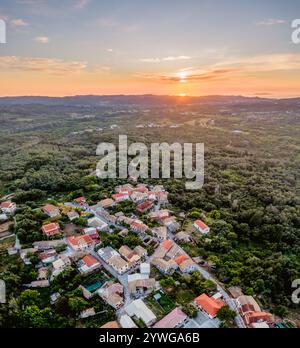 Vue aérienne sur le coucher du soleil d'un village pittoresque niché au milieu d'une végétation luxuriante. Banque D'Images