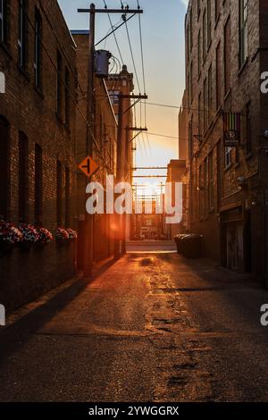 Une ruelle étroite avec un panneau jaune pointant vers la gauche. Le soleil se couche, projetant une lueur chaude sur les bâtiments en briques Banque D'Images