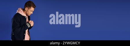 Jeune homme se tient dans la pensée profonde sur un fond bleu solide. Banque D'Images