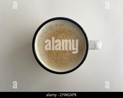 Vue de dessus d'un café mousseux dans une tasse minimaliste mouchetée sur fond blanc Banque D'Images