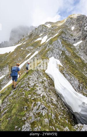 Deux alpinistes avec des casques sur un sentier de randonnée étroit, ascension à l'Ackerlspitze, nuages se déplaçant autour des montagnes, Wilder Kaiser, Kaiser Mountain Banque D'Images