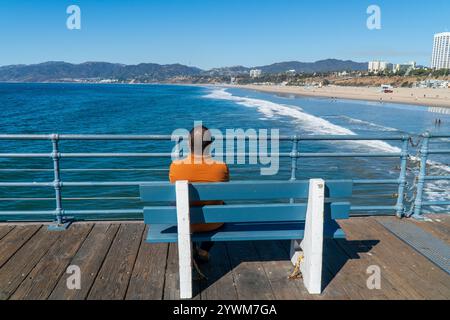 Un homme regardant vers la plage de Santa Monica et les collines du comté de Los Angeles, assis sur un banc sur la jetée de Santa Monica Banque D'Images