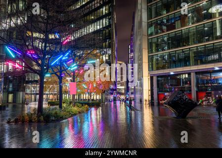 Arbres décorés de lumières de Noël colorées le long d'un sentier qui court entre des immeubles de bureaux en verre la nuit Banque D'Images