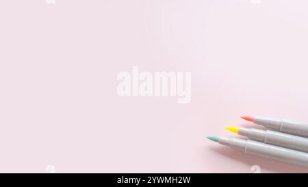 Trois stylos à pinceau colorés sont placés dans le coin d'un fond rose - matériel d'image avec espace de copie pour étudier, dessiner ou diversité. Banque D'Images