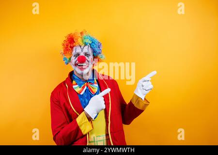 Clown souriant pointant, fond jaune vif, plaisir. Banque D'Images