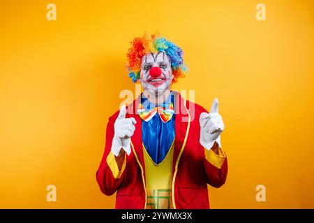 Clown souriant pointant, fond jaune vif, plaisir. Banque D'Images