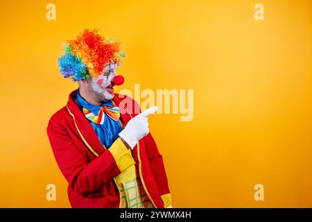 Clown souriant pointant, fond jaune vif, plaisir. Banque D'Images