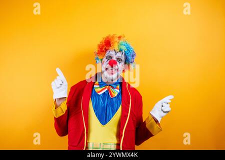 Clown souriant pointant, fond jaune vif, plaisir. Banque D'Images