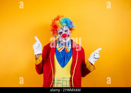 Clown souriant pointant, fond jaune vif, plaisir. Banque D'Images