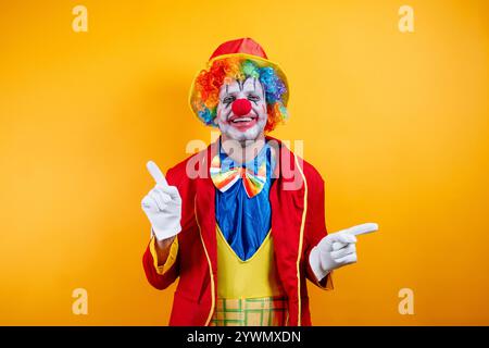 Clown souriant pointant, fond jaune vif, plaisir. Banque D'Images