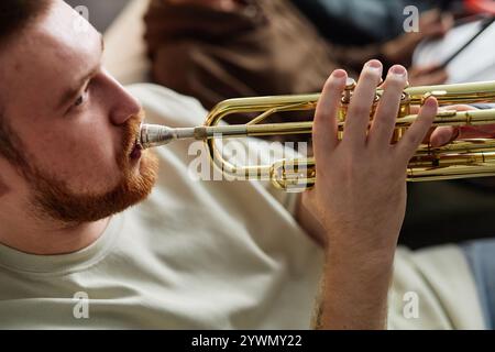 Vue latérale gros plan de l'homme aux cheveux rouges jouant de la trompette à la maison avec l'accent sur les mains pressant les valves, espace de copie Banque D'Images